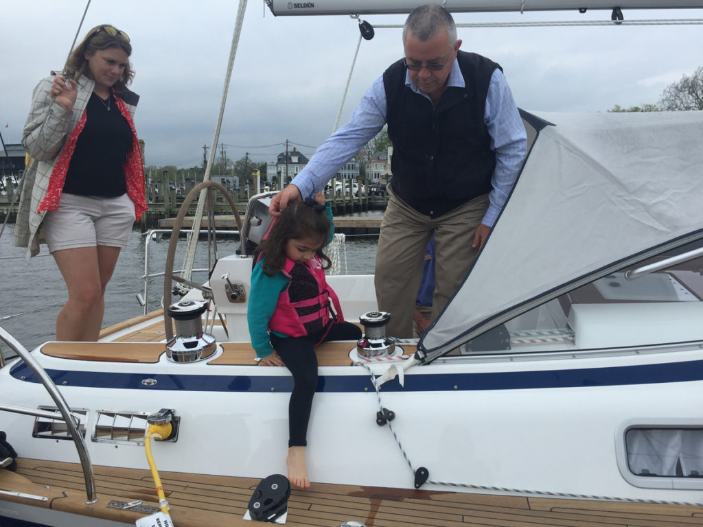 A lady, a man, and a little girl on a sailing boat. The man is helping the girl get off the boat.