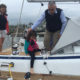 A lady, a man, and a little girl on a sailing boat. The man is helping the girl get off the boat.